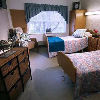 A cozy bedroom featuring two neatly made beds, decorated with floral and solid color linens, alongside a window with curtains.