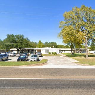 A single-story building with a parking lot and several cars, situated alongside a road on a clear day.