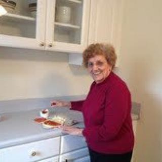 A woman in a kitchen smiling as she cuts a cake.