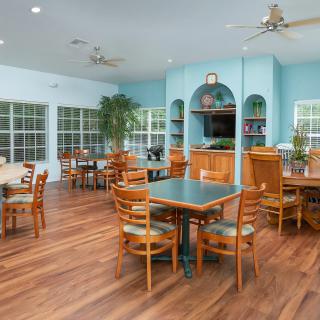 A cozy indoor dining area with wooden floors, tables, and chairs, featuring a bookshelf and ceiling fans.