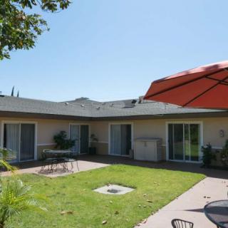 A sunny backyard with a patio, lawn, and outdoor furniture shaded by a large umbrella.