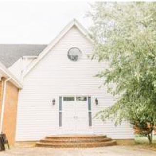 A charming white house with a gabled roof and brick steps leading to the entrance, flanked by trees.