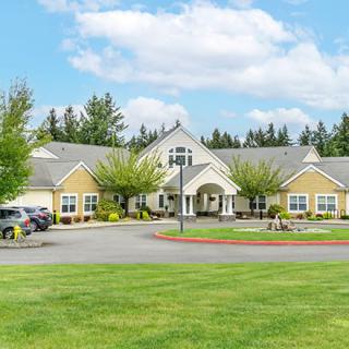 A picturesque residential building surrounded by a lush green lawn and trees, with a clear blue sky above.