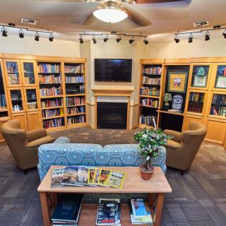 A cozy library reading area with bookshelves, a sofa, chairs, and a television.