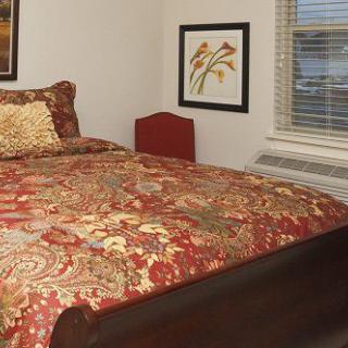 A cozy bedroom with a patterned comforter and framed artwork on the wall.