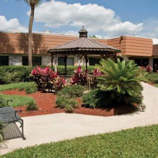 A well-maintained garden with a central gazebo, surrounded by vibrant plants and a paved pathway.