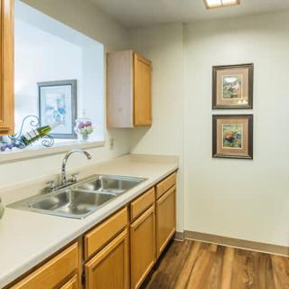 A clean and tidy kitchen with wooden cabinets, a double sink, and wood flooring.