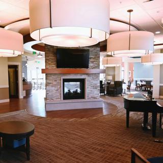 A spacious and modern lounge area featuring a central fireplace, stylish lighting, and a grand piano.
