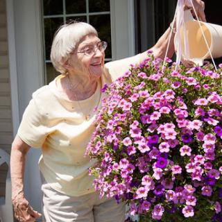 An elderly woman joyfully tending to her vibrant hanging flower basket.