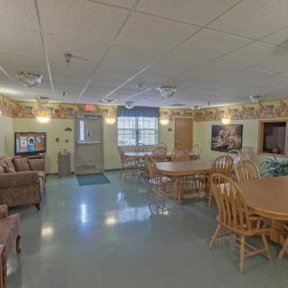 A well-lit community dining and living area with wooden tables and chairs, decorated walls, and a comfortable seating arrangement.