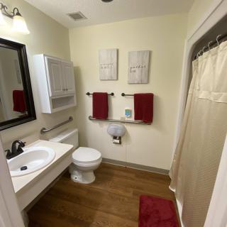A well-organized bathroom featuring a sink, toilet, and shower with red towels and wooden flooring.
