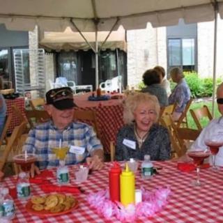 A group of seniors enjoying a picnic under a tent with checkered tablecloth.