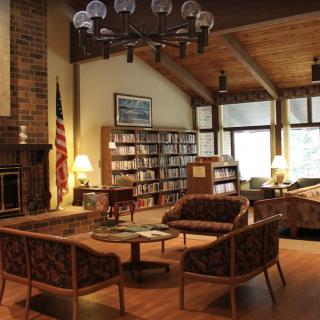 A cozy library interior with a seating area, bookshelves, a fireplace, and warm lighting.