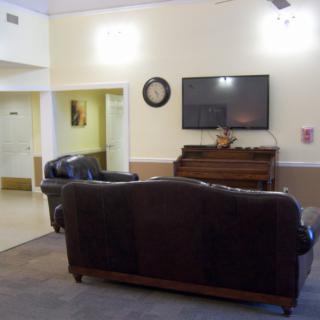 A cozy living room featuring a sofa set, wall-mounted television, and a piano.