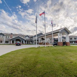 A large building with several flags out front, surrounded by a well-maintained lawn and set against a cloudy sky.