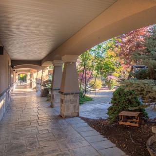 A covered walkway with columns and landscaped gardens on a sunny day.