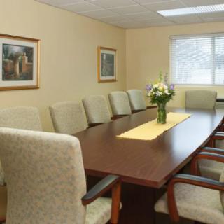 A well-appointed conference room with a long meeting table and upholstered chairs, featuring a decorative flower arrangement and framed artwork on the walls.