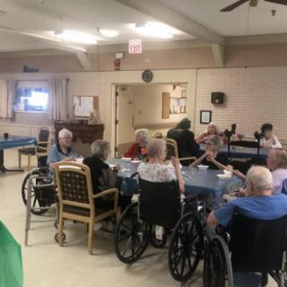 A group of elderly people in wheelchairs gathered indoors at a nursing home.