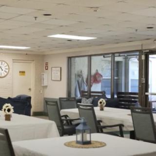 An indoor dining area with neatly arranged tables and chairs, a wall clock, and ceiling lights.
