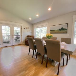 A bright and inviting dining room featuring a modern table set for meals, surrounded by comfortable seating.