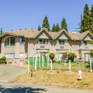 A large suburban house with a fenced yard and surrounding trees.