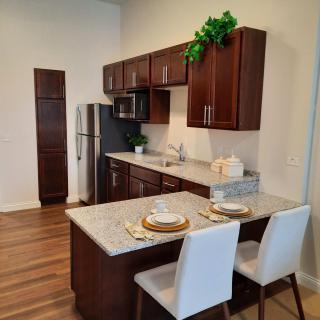 A modern kitchen with wood cabinetry, stainless steel appliances, and a marble countertop with bar seating.