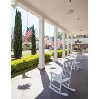 A sunny porch with rocking chairs and American flags in a well-maintained garden setting.