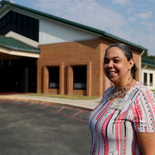 A woman stands smiling in front of a building during the daytime.