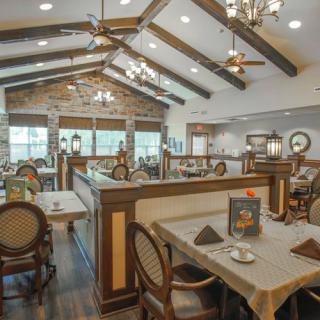 A spacious and elegantly designed restaurant interior with wooden beams, chandeliers, and neatly arranged tables and chairs.
