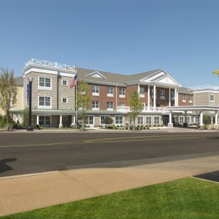 A three-story building with a classical design, featuring white columns and brick details, located alongside a road.