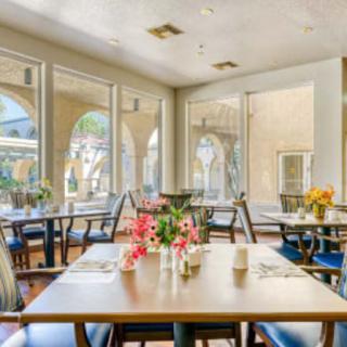 A bright and welcoming restaurant interior with tables decorated with flowers, surrounded by large windows.