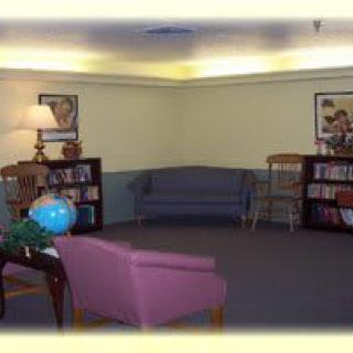 A cozy library lounge area with bookshelves, a sofa, chairs, and a lamp.