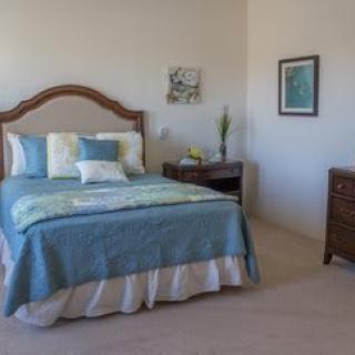 A cozy bedroom featuring a neatly made bed with blue and white bedding, accompanied by wooden furniture and decorative artwork on the walls.