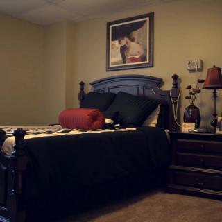 A cozy bedroom with a neatly made bed, decorative pillows, a nightstand with a lamp, and artwork hanging above the headboard.
