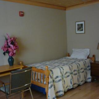 A simple bedroom with a single bed, wooden desk, and a vase of pink flowers.