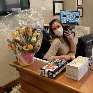 A receptionist at the desk in an office, wearing a mask and surrounded by a colorful bouquet of flowers.