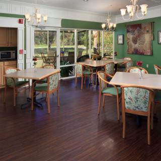 A cozy dining area with multiple tables and chairs, featuring a hardwood floor and large windows.