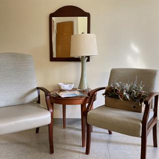 A cozy seating area featuring two chairs, a small table with a plant arrangement, and a lamp reflecting the warm ambiance of the room.