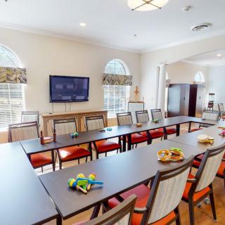 A well-lit conference room with long tables, chairs, and a television.
