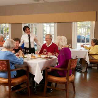 A group of seniors enjoying a meal together in a restaurant with a server attending to their table.