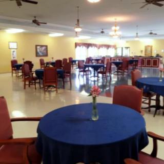 An empty dining area with tables covered in blue tablecloths and a vase with flowers on each table.