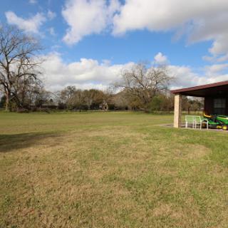 A serene outdoor space featuring a grassy area, trees in the background, and a building partially shaded by clouds.