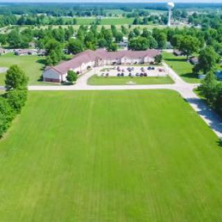 Aerial view of a green field with a building surrounded by trees in a suburban area.