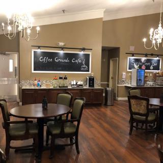 A cozy cafe interior featuring tables, chairs, chandeliers, and a coffee station.