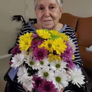 An elderly woman in a wheelchair proudly holds a beautiful bouquet of colorful flowers.