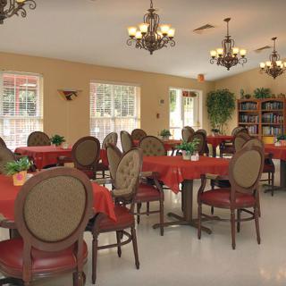 A spacious dining room with elegantly set tables and chairs, adorned with chandeliers and large windows.