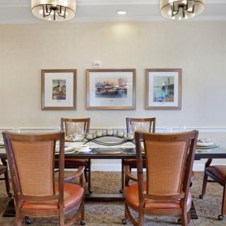 A well-decorated dining room with a wooden table, leather chairs, artwork on the wall, and elegant lighting.