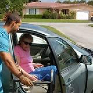 A caregiver helps an elderly woman transfer from a car to a wheelchair.