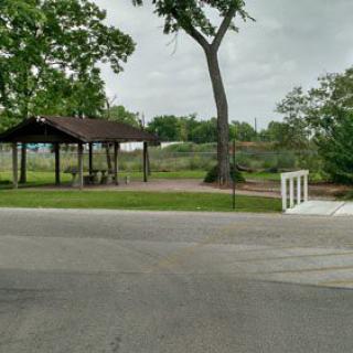 A small park area with a pavilion, surrounded by trees and greenery, featuring a white bridge over a walkway.