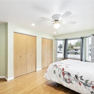 A bright bedroom with wooden floors, a ceiling fan, and a large window allowing natural light.